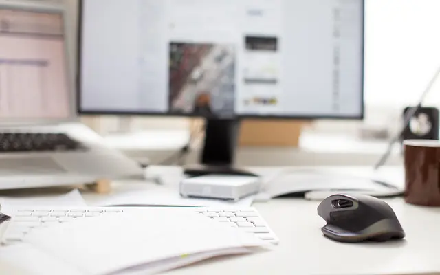 Office desk with monitor, white keyboard, wireless mouse and printed documents
