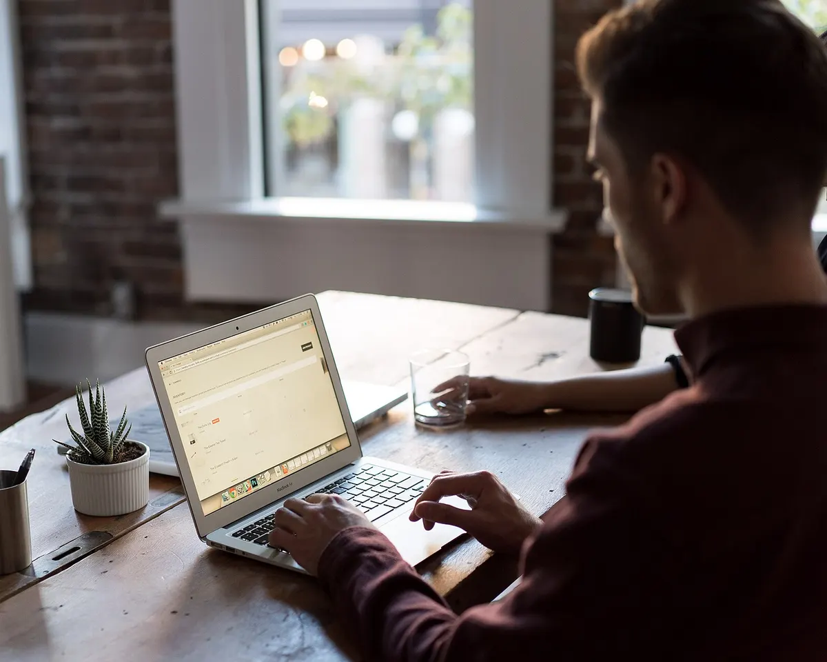 Man typing on a laptop at a wooden desk in a bright office