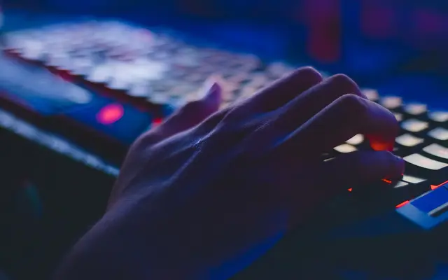 Hand typing on a dark keyboard lit by red and blue light