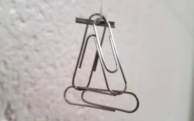 Silver paperclips hooked together hanging against a pale wall