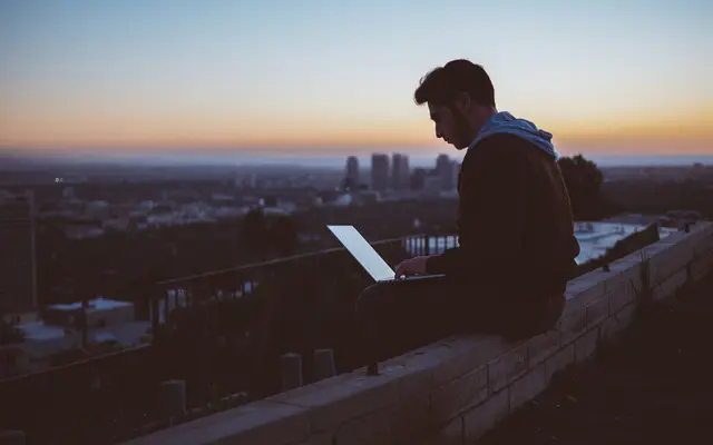 Person working on a laptop outdoors at dusk above a city