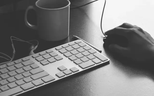 Hand resting on a computer mouse beside a keyboard on a desk