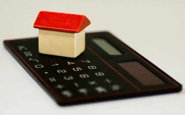 Small wooden toy house sitting on top of a black calculator