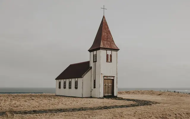 Small white wooden church with a steeple under a grey sky